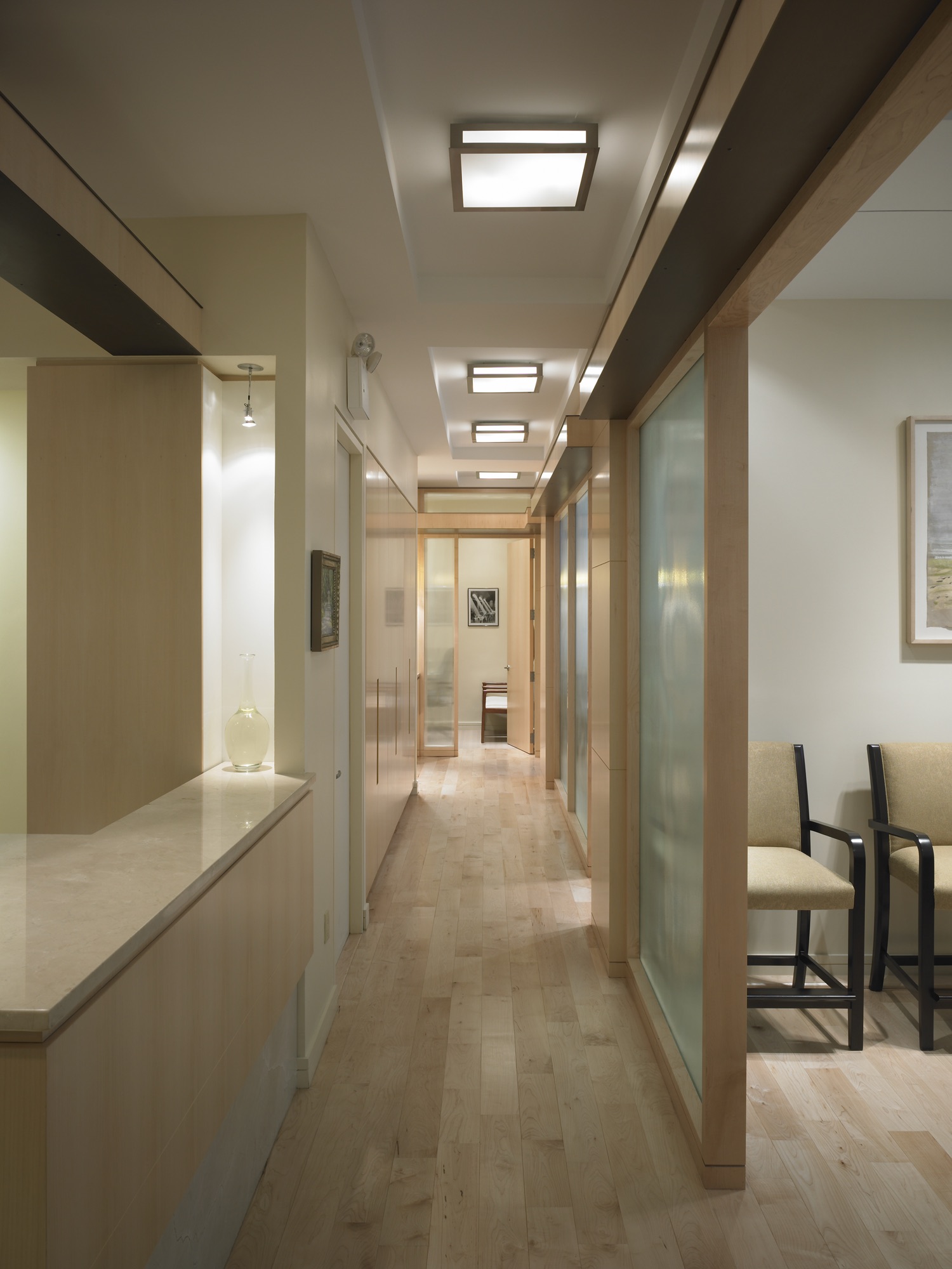 Medical office circulation with dark charcoal columns, herringbone oak floor, and green marble reception counter